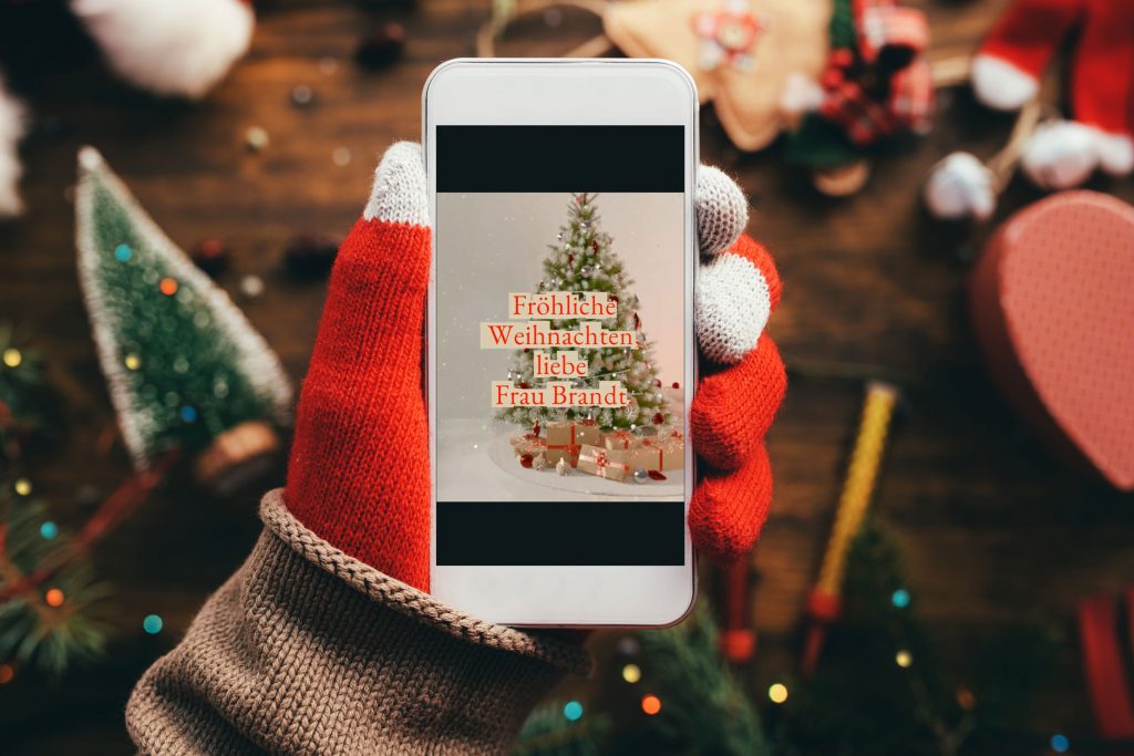 Hand mit Smartphone darauf digitale Weihnachtskarte für Kunden und Geschäftspartner.